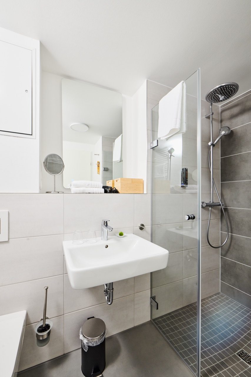 Badezimmer mit großem Spiegel, Waschbecken und ebenerdiger Dusche mit Glaswand